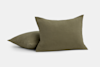 Two olive green, textured square pillows are placed on a plain, light background. One pillow is standing upright, while the other is lying flat behind it.