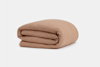 A neatly folded light brown blanket with a subtle textured pattern, placed on a plain white background.