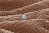 A close-up of a textured, light brown fabric with wavy, stitched lines, featuring a single white four-hole button sewn onto it.