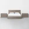 A minimalist bedroom featuring a wooden bed frame with white bedding and two matching wooden nightstands, all set against a plain white wall and a light gray floor.