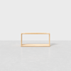 A minimalist, rectangular wooden shelf with open sides sits on a light gray floor against a plain white background.