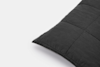 A close-up of a dark gray quilted pillow on a white background, showing the stitched seams and soft fabric texture.