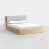 A modern wooden bed frame with a light wood finish, featuring a cushioned gray headboard and neatly made with white bedding and two pillows, set against a plain white background.