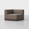 A modern, brown, L-shaped corner chair with a low back and wooden base, set on a light grey floor against a plain white background.
