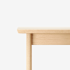 Close-up of the corner of a light-colored wooden table against a white background.