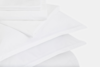 A neatly stacked set of white bed sheets and pillowcases arranged on a white surface, showcasing smooth and crisp fabric.