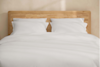 A neatly stacked set of white bed sheets and pillowcases arranged on a white surface, showcasing smooth and crisp fabric.