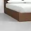 A close-up of a wooden platform bed with white bedding and pillows, set on a light gray floor against a plain white wall.