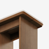Close-up view of the corner of a wooden table with a light-colored, rounded-edge tabletop and sturdy vertical legs, set against a white background.