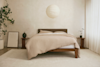 Minimalist bedroom with a wooden bed, beige bedding, a round paper lantern light, two small nightstands, potted plants, framed art on the floor, and soft natural light through sheer curtains.