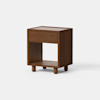 A wooden nightstand with a single drawer and an open lower shelf, standing on four short cylindrical legs, displayed against a plain white background.