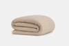 A neatly folded, beige quilted blanket is displayed against a plain white background.