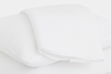 A neatly folded white bedsheet rests on top of a white pillow, both on a white surface, creating a clean and minimal look.