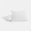Two white pillows with textured covers are placed on a plain white background; one pillow is upright while the other lies flat beneath it.