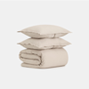Two beige pillows stacked neatly on top of a folded beige comforter, all set against a plain white background.