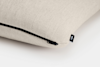 Close-up of a beige fabric cushion with a visible black zipper along the seam and a small black fabric tag with white text that reads MUJI. The background is plain white.