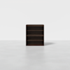 A dark brown wooden bookshelf with three shelves stands centered on a light gray floor against a plain white background.