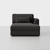 A modern dark gray chaise lounge with a low backrest, a single armrest on the right, and a rectangular pillow, set against a plain light gray background.