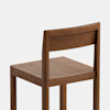 A simple wooden chair with a flat seat, straight backrest, and square legs, shown against a plain white background. The chair has a minimalist design and a natural wood finish.
