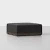 A modern square ottoman with a dark gray upholstered cushion and a wooden base, placed on a light floor against a plain white background.