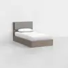 A single bed with a wooden frame and a padded gray headboard, dressed in white bedding and a pillow, placed in a minimal, empty room with light walls and floor.