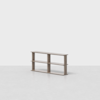 A minimalist, light wood bookshelf with three open compartments, standing on a light grey floor against a plain white background. The bookshelf has two shelves and a simple, modern design.