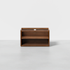 A square, open-front wooden cabinet with a single shelf and an empty top compartment, placed on a plain gray floor against a white background.
