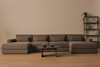 A modern living room with a large brown sectional sofa, a round wooden coffee table with two small items on it, and a tall black shelf holding plants and decorative objects against a beige wall.