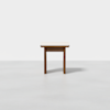 A small, simple wooden stool with four legs and a rectangular seat, placed on a light gray floor against a plain white background.