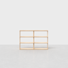 A minimalist wooden shelving unit with six open rectangular compartments, standing on a smooth, light gray floor against a plain white background.