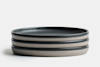 Three stacked, round ceramic plates with a matte gray exterior and a dark, almost black, interior, set against a plain white background.