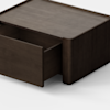 A dark wooden rectangular drawer unit sits on a light gray floor with one drawer partially open, against a plain white background.