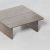 A modern, minimalist wooden coffee table with a rectangular top and two wide, flat legs on each end, set against a plain light background.