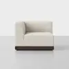 A modern, armless beige sectional sofa piece with textured fabric and a dark wooden base, shown against a plain light gray background.