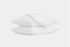 Two stacked white pillows with a neatly folded white blanket resting on top, all set against a plain white background.