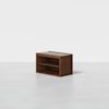 A small, rectangular wooden cabinet with an open front featuring two shelves, placed on a white floor against a plain white background.