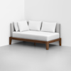 A modern daybed with a wooden frame and light gray upholstered back and side rests, topped with three large white pillows, placed in the corner of a minimalist room with light flooring and white walls.