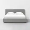 A modern bed with a gray upholstered frame, white sheets, and two white pillows, positioned against a plain white wall in a minimalistic room.