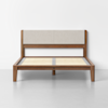 A modern wooden bed frame with a beige upholstered headboard, slatted wooden base, and clean, minimalist design, set against a plain white wall and gray floor.