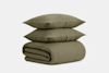 Two olive green pillows are stacked on top of a matching folded comforter, all made of textured fabric, against a plain light gray background.