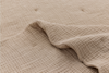 A close-up view of a beige, textured, waffle-knit fabric blanket, with one corner slightly folded over, revealing the soft and cozy material.
