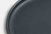 Close-up of a dark gray, round plate with a slightly raised edge, shown against a white background. Only part of the plate is visible in the image.