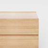 A close-up view of a light wooden dresser or cabinet with clean, minimalist lines, shown against a plain white background.