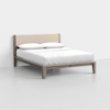 A modern wooden bed with a beige upholstered headboard, white bedding, and two white pillows, set against a plain white wall and floor.
