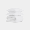 Two white pillows stacked on top of a neatly folded white comforter, all set against a plain white background.