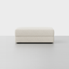 A rectangular, light beige upholstered ottoman is set against a plain white background with a smooth gray floor. The design is simple and modern, with no visible legs or decorative elements.