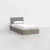 A single bed with a gray upholstered headboard, white bedding, and a light wooden frame sits in a minimal, empty white room.