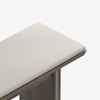 A close-up view of the corner of a bench with a light beige upholstered cushion and a wooden frame, shown against a plain white background.