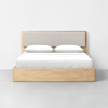 A minimalist wooden bed with a light beige upholstered headboard, two white pillows, and white bedding, placed against a plain white wall on a gray floor.