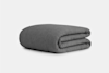 A neatly folded, dark gray blanket with a textured surface is placed on a plain, light gray background.